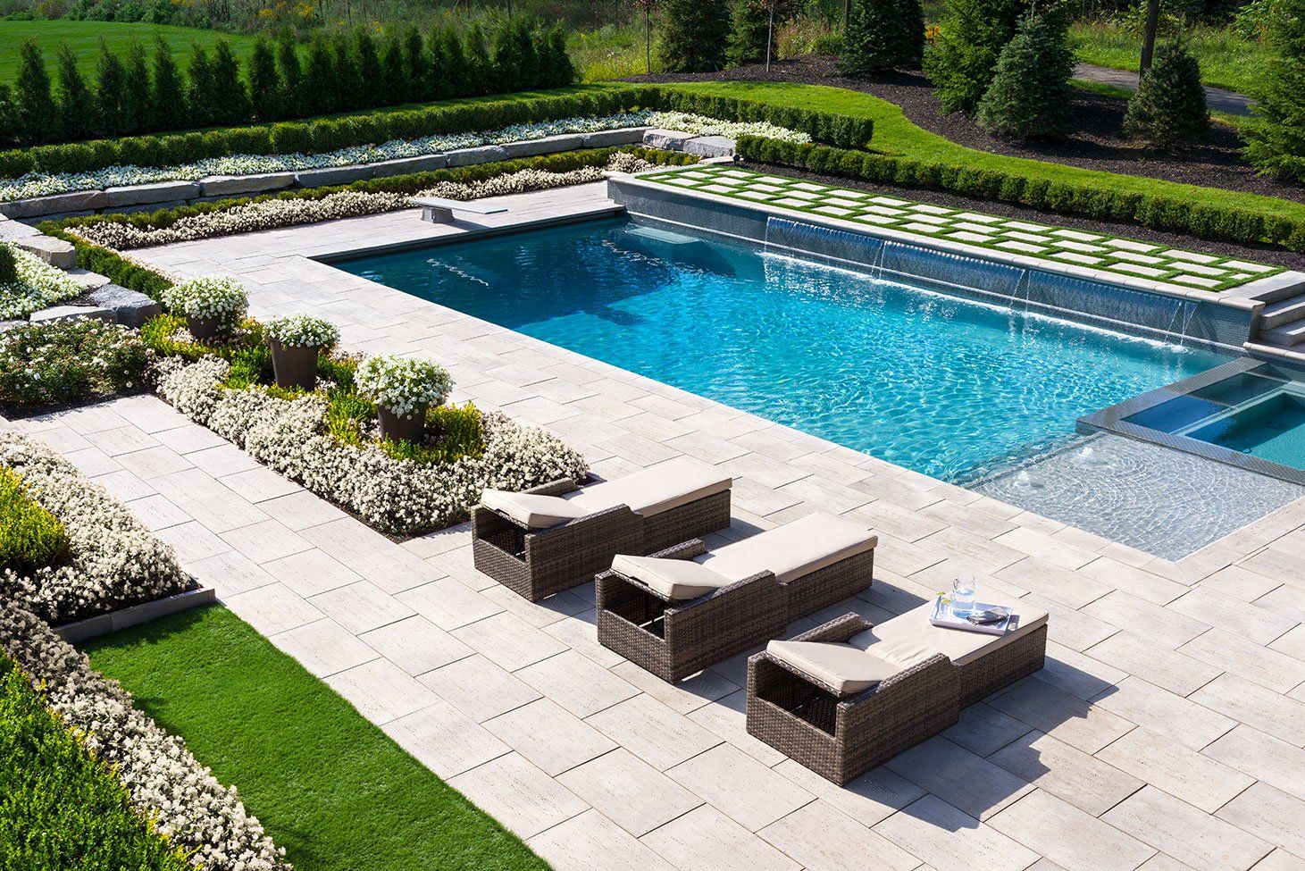Outdoor pool with lounge chairs, surrounded by greenery and stone patio.