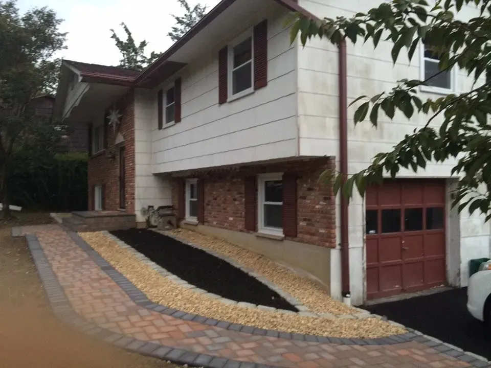 Two-story house with brick accents, driveway, and paved walkway. Brown garage door and red shutters.