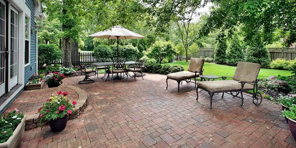 Brick patio with outdoor seating, umbrella, and lush greenery.