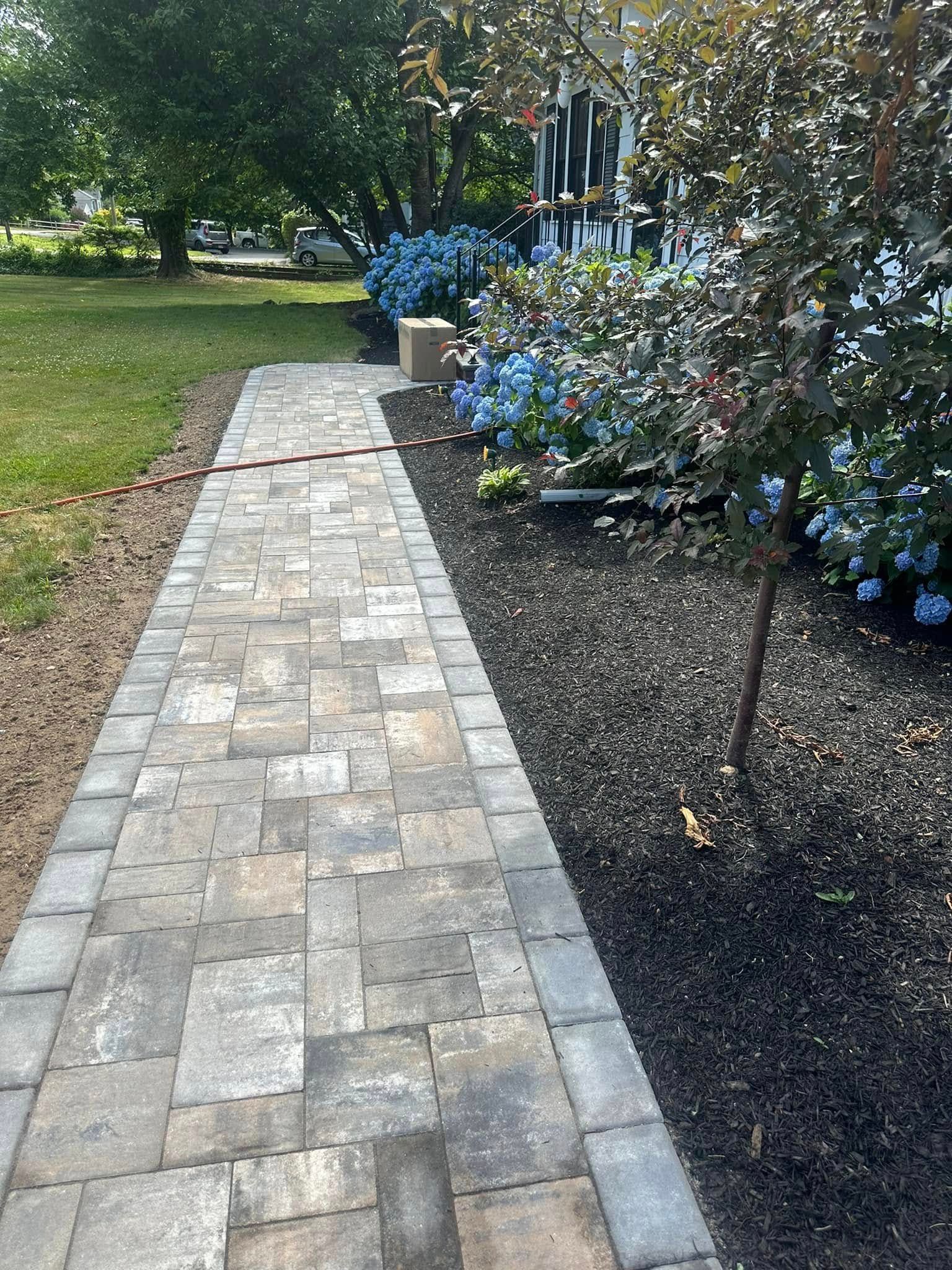 Stone walkway bordered by mulch and flowers, leading to a house.