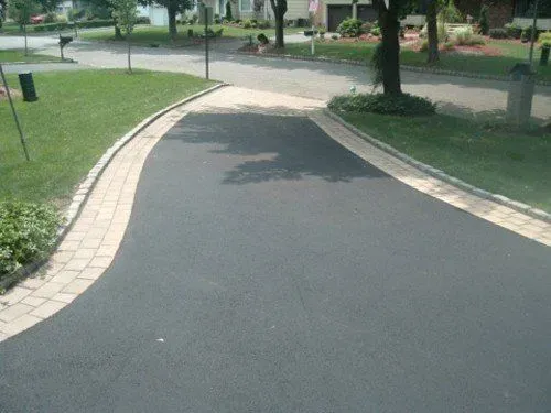 Asphalt driveway with tan brick edging, bordering grass and a residential street.