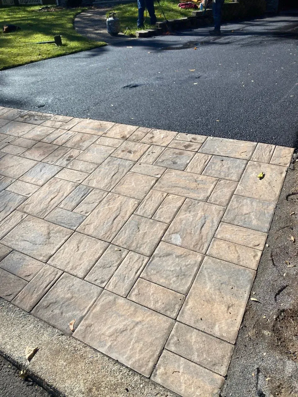 Paver driveway section adjoins asphalt driveway. Light brown paving stones and dark gray asphalt.