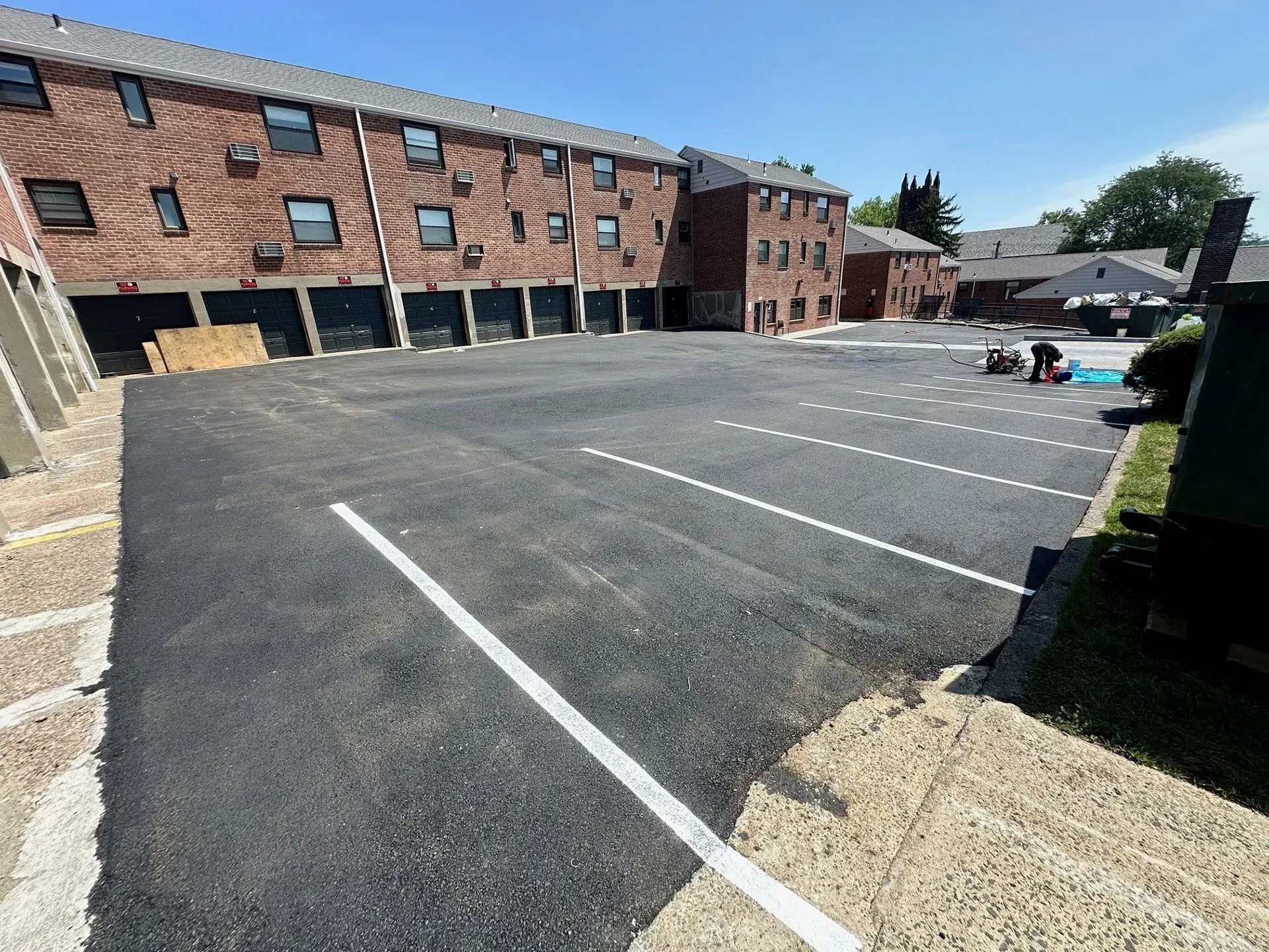 Newly paved parking lot with white lines, in front of a brick apartment building.