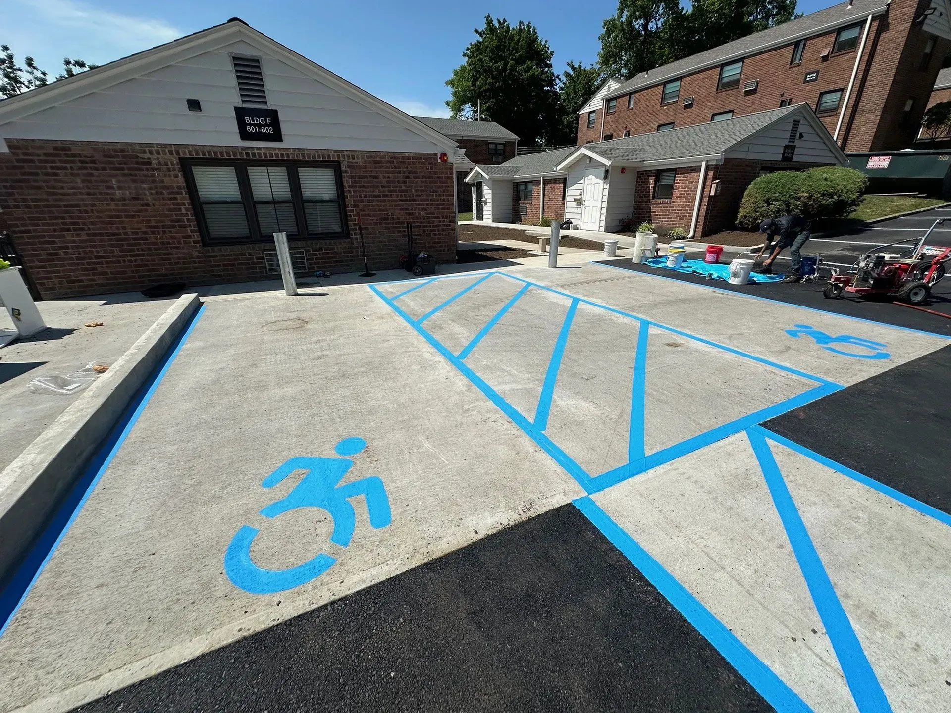 Parking lot with newly painted blue disabled parking symbols and lines. Buildings in background.