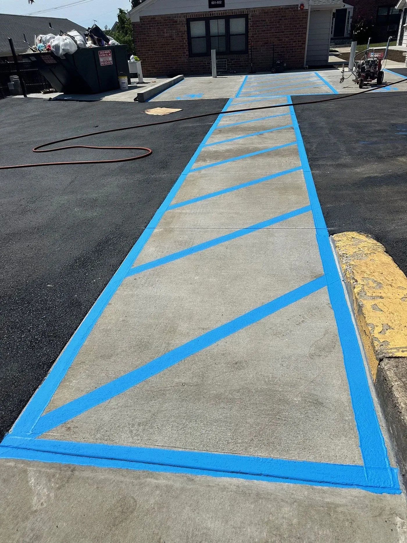 Blue-striped concrete walkway in a parking lot, leading to a building.