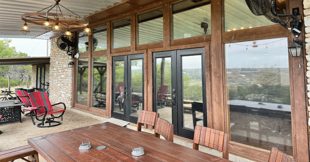 A large patio with a wooden table and chairs and a lot of windows.