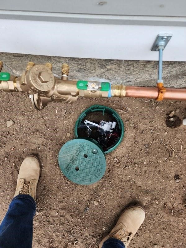 A person is standing next to a water meter on the ground.