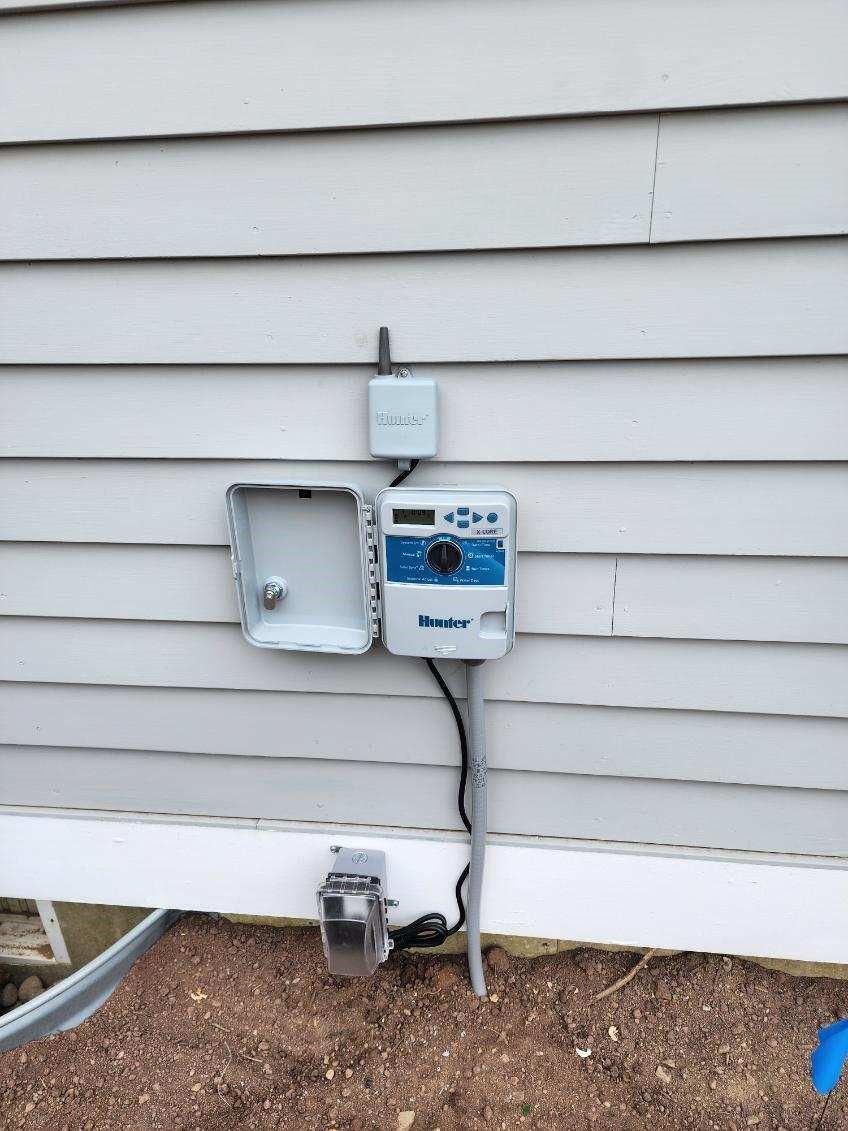 A sprinkler controller is attached to the side of a house.