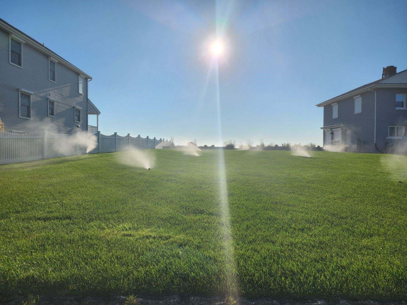 A lawn is being watered by a sprinkler on a sunny day