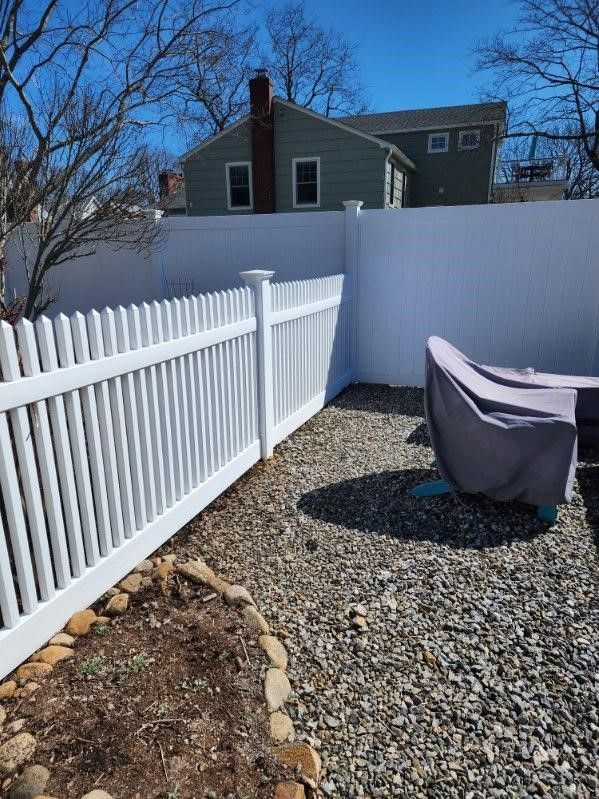 A white picket fence surrounds a gravel area in a backyard.