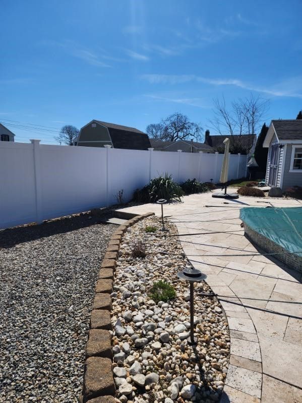 A white fence surrounds a backyard with a patio and a pool.