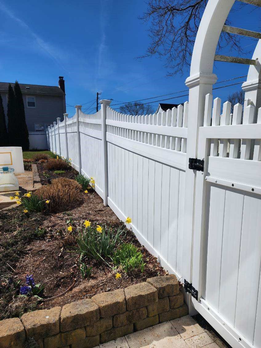 A white fence with a gate in the middle of a garden.