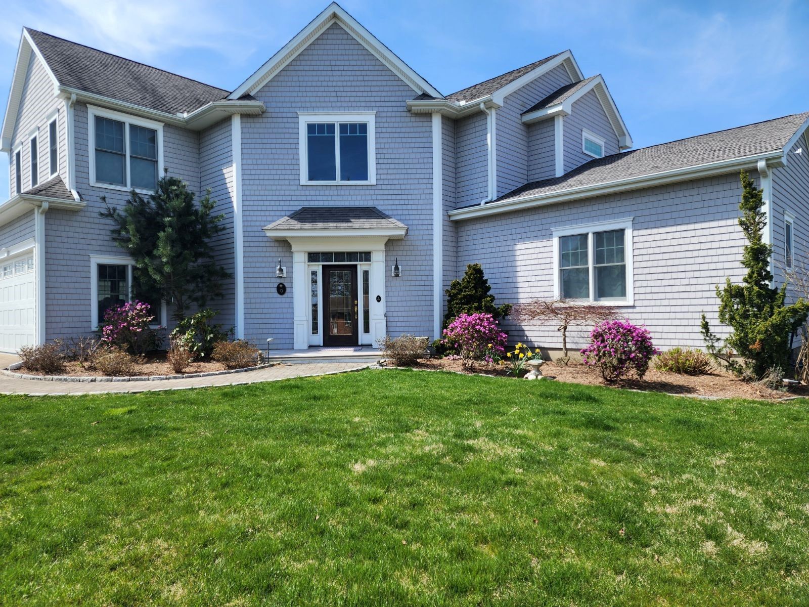 A large gray house with a lush green lawn in front of it.