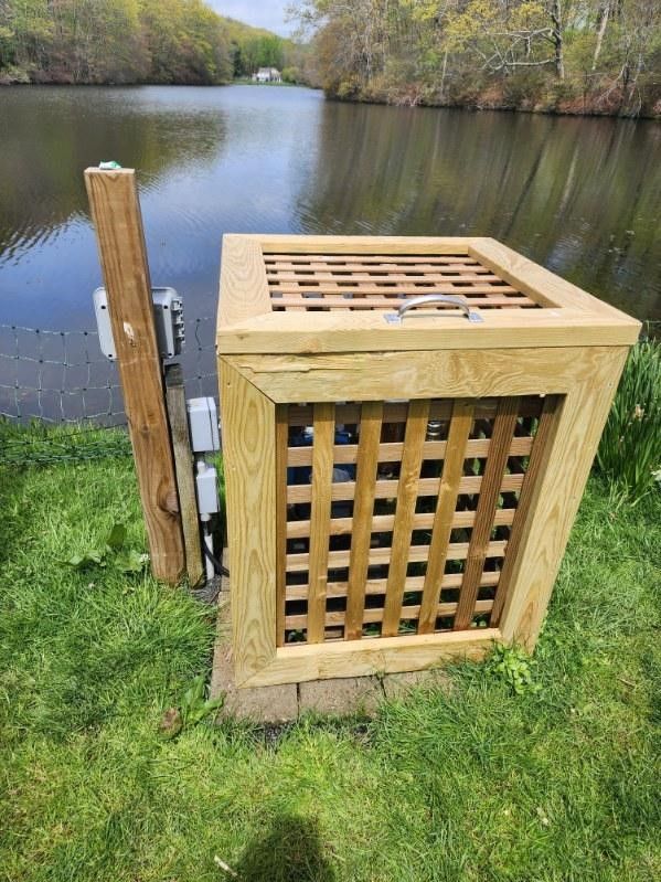 A wooden box is sitting in the grass next to a lake.