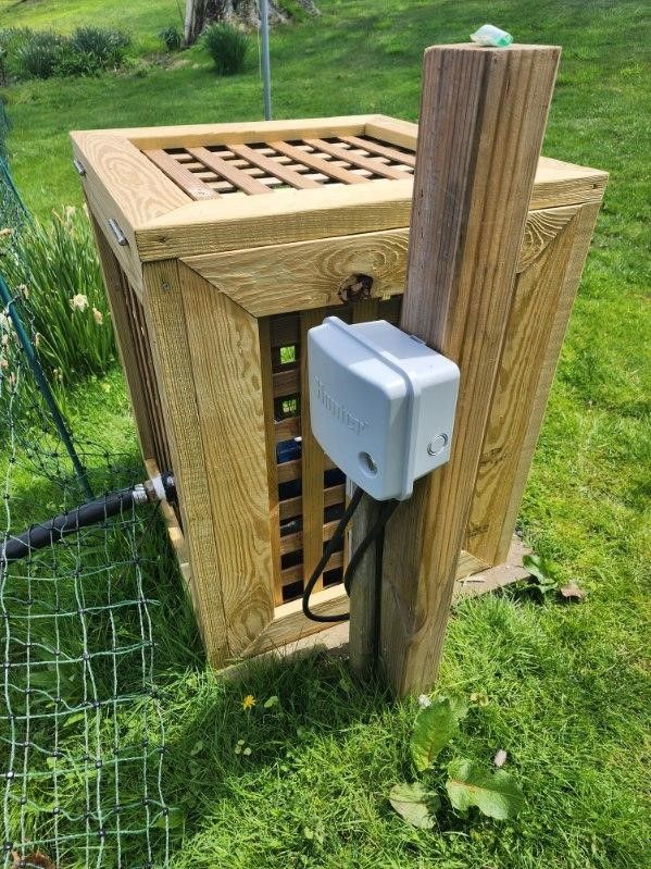 A wooden box is attached to a wooden post in the grass.