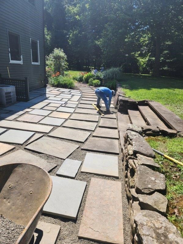 A man is working on a stone walkway in a backyard.