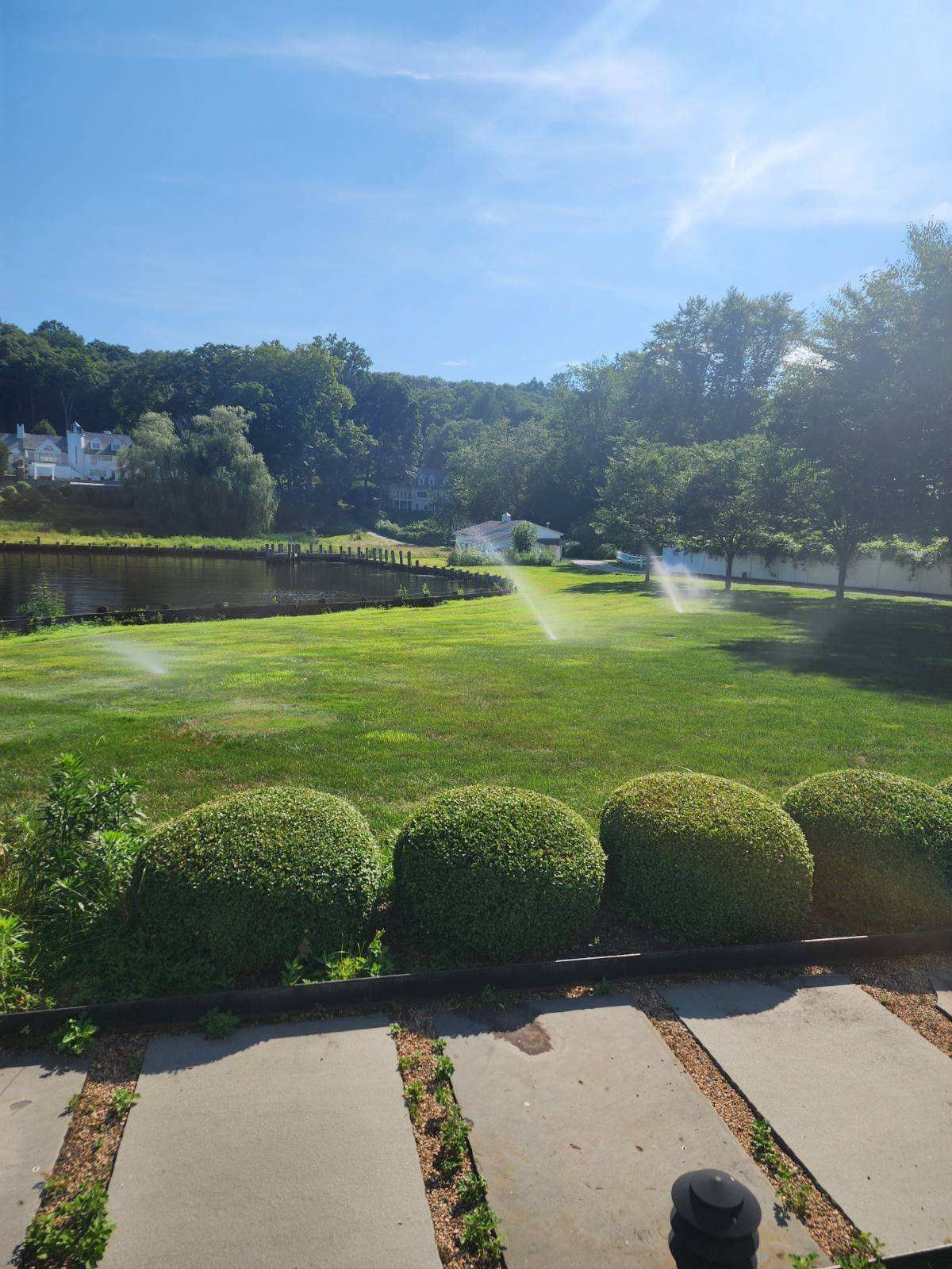 A lawn with sprinklers spraying water on it on a sunny day.