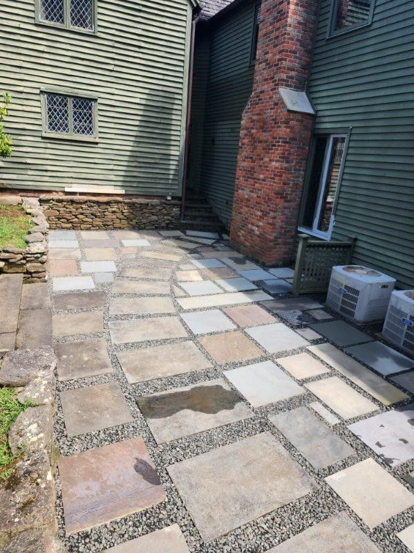A stone walkway leading to a house with a brick chimney.