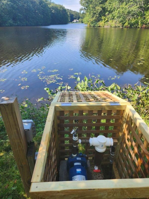 A wooden box with a pipe inside of it is next to a lake.