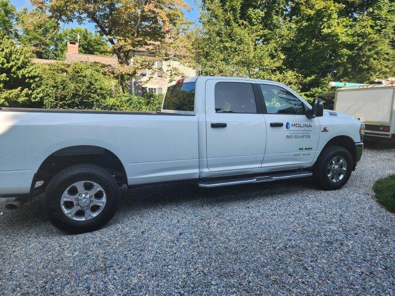 A white pickup truck is parked on gravel in front of a house.