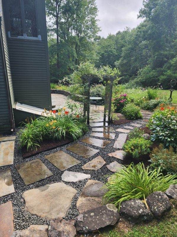 A stone walkway leading to a house in a garden.