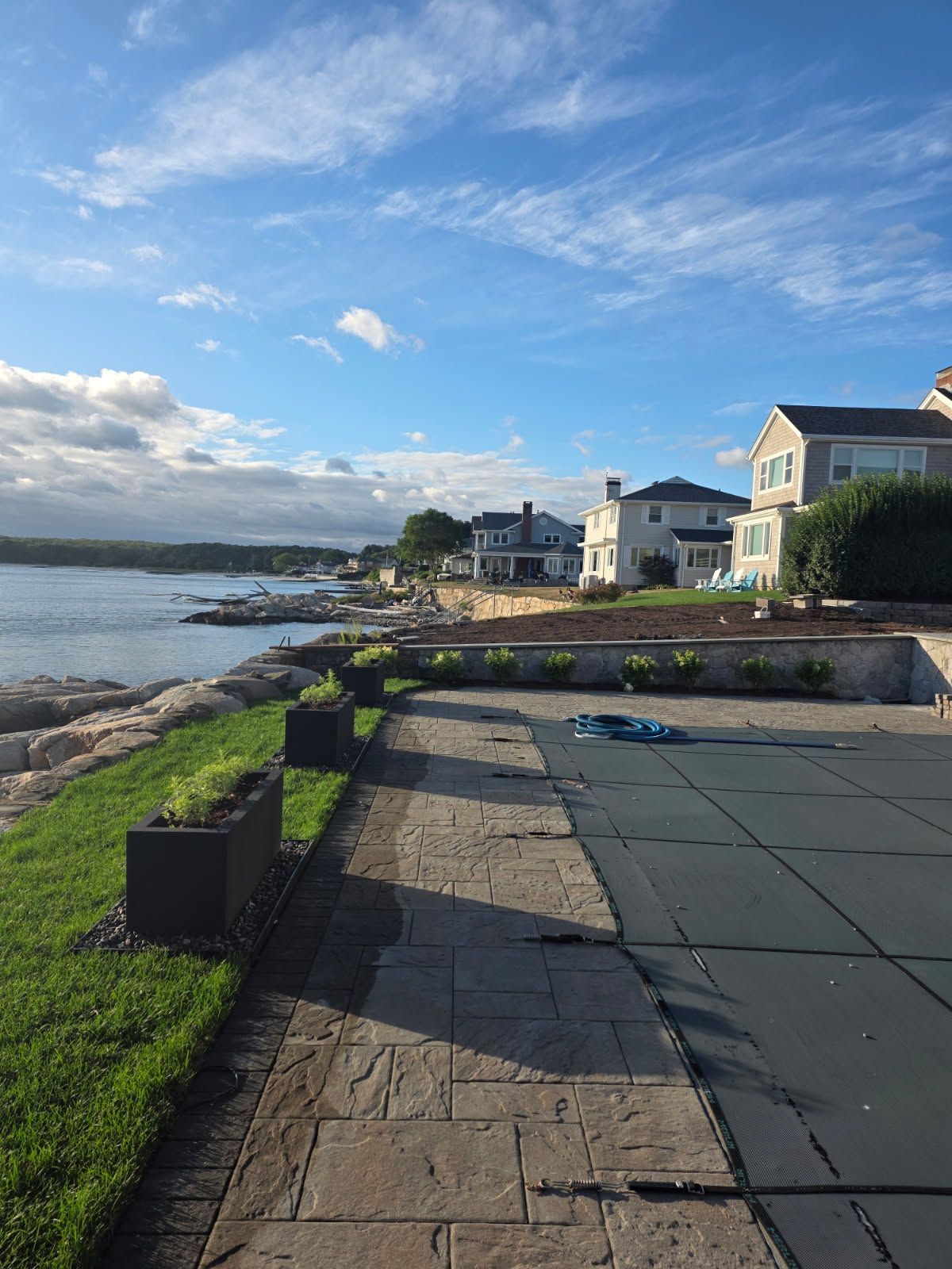 Lakeside view with homes, water, blue sky, green grass, and a covered pool.