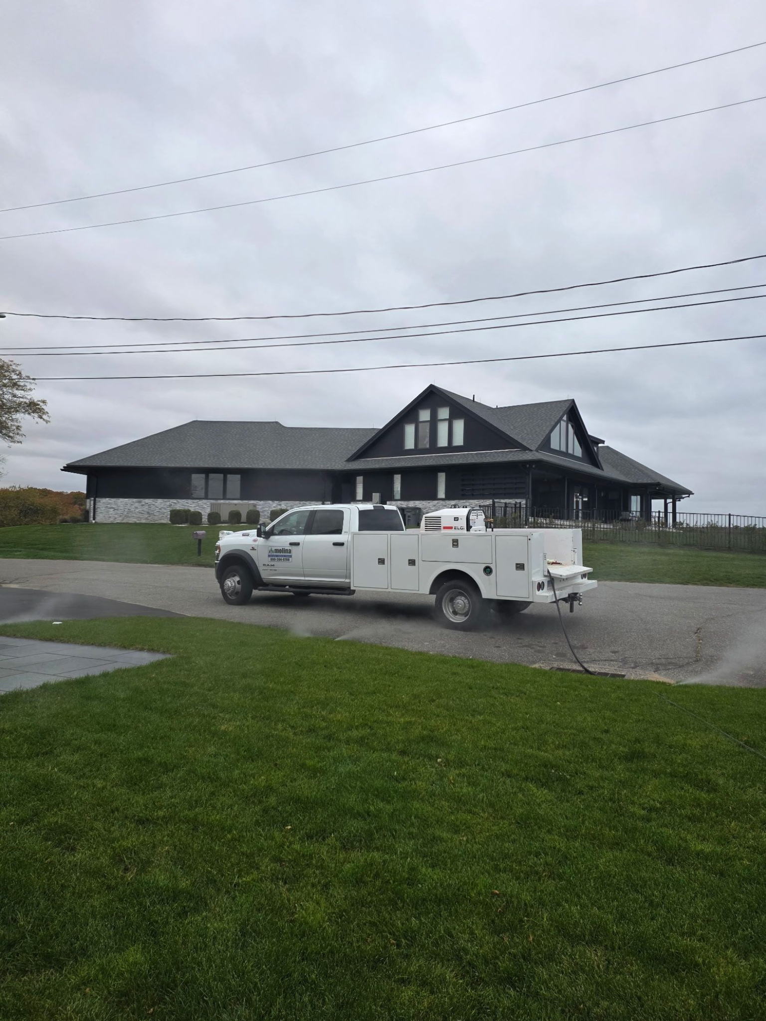White work truck parked in front of a modern house on a cloudy day.