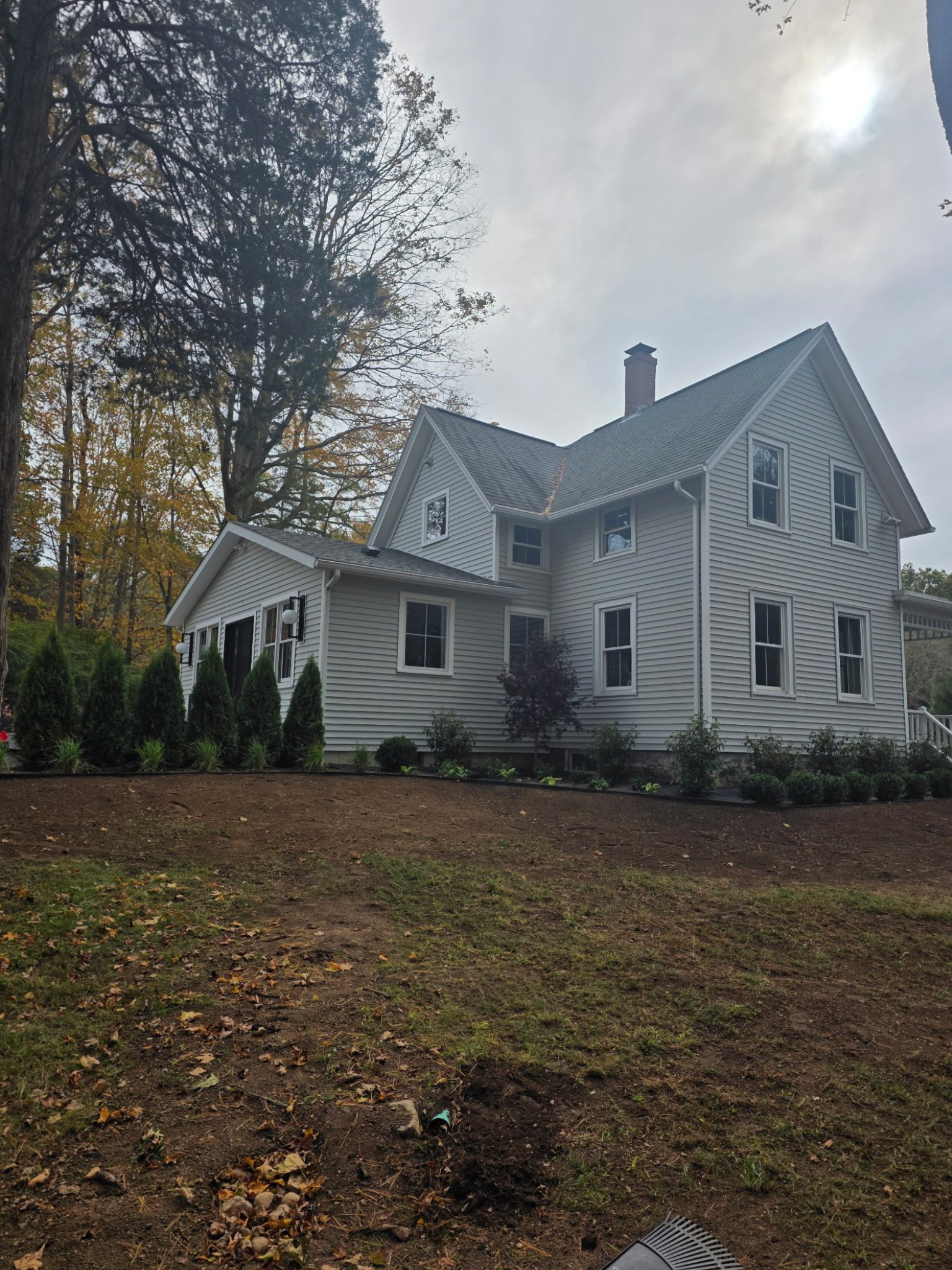 White house with gray siding, two stories, chimney, and landscaped yard. Overcast sky.