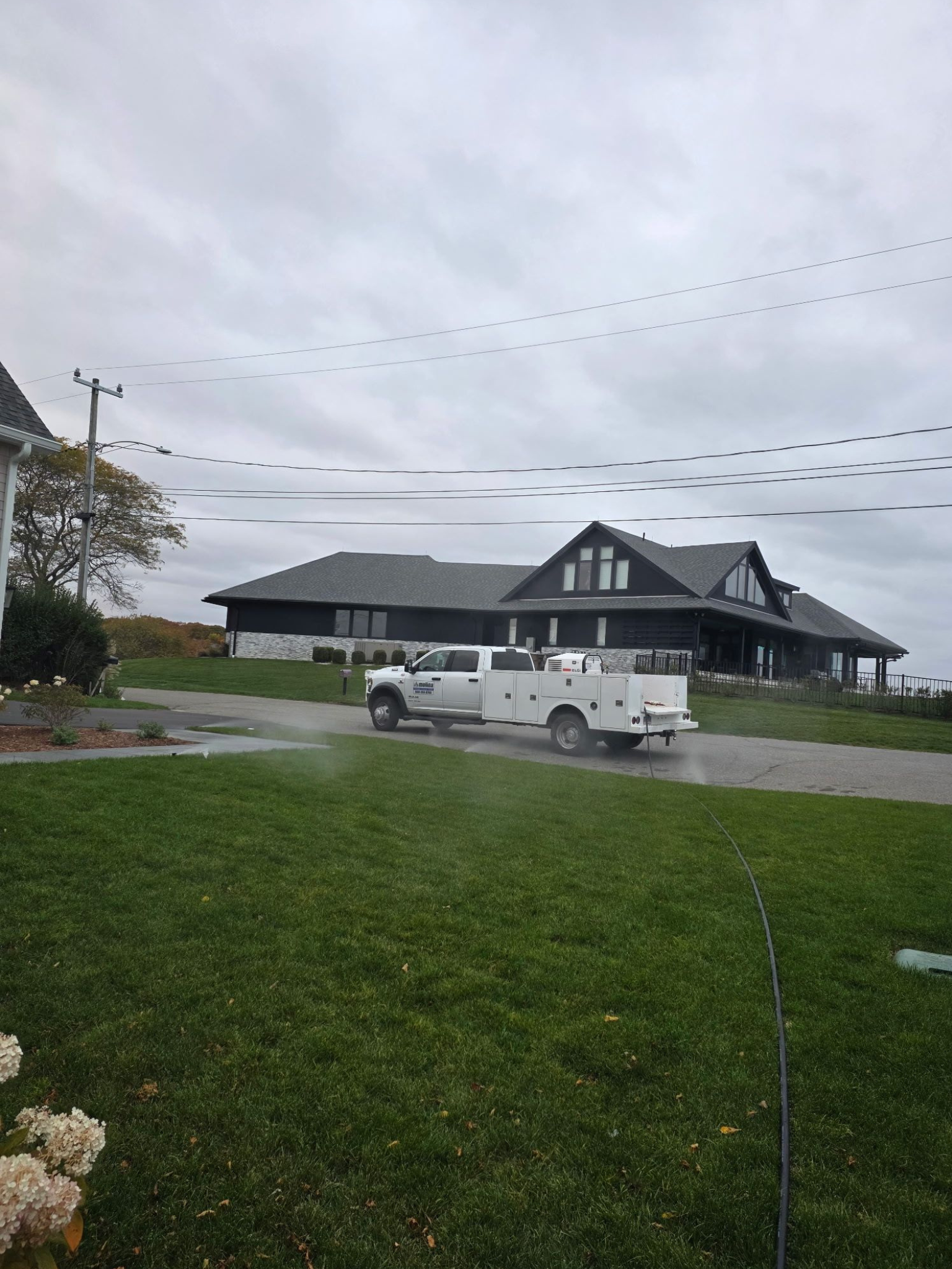 White work truck parked on a green lawn in front of a large house under an overcast sky.