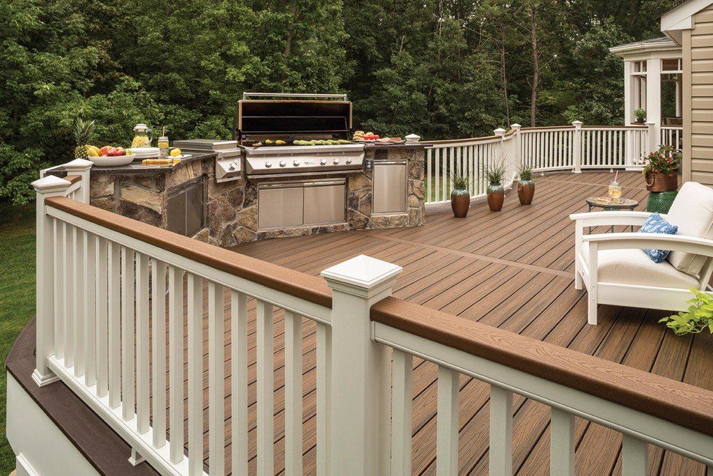 Wooden deck with railing, grill, and white chairs in a backyard