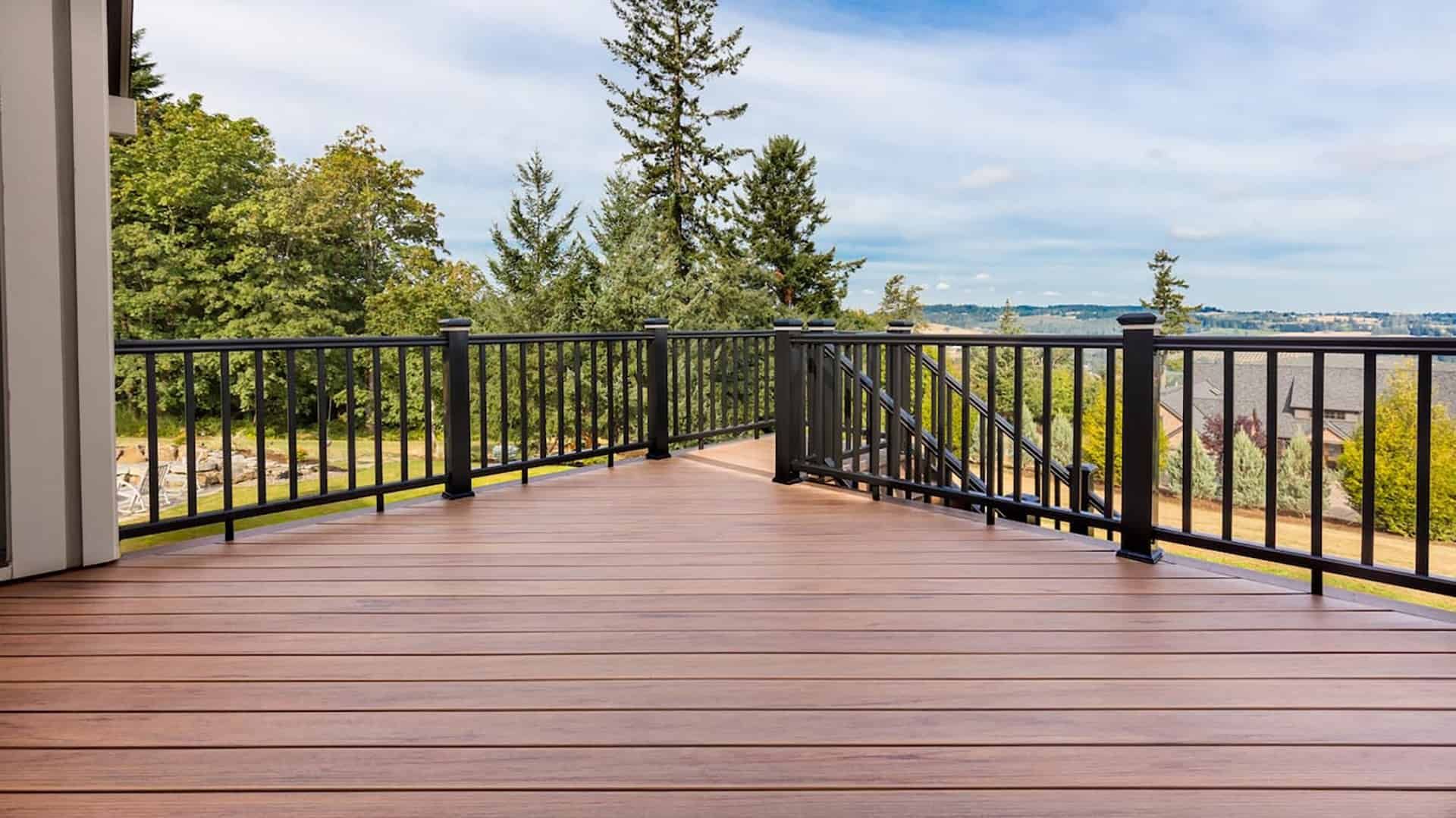 Wooden deck with black railings overlooking green trees and a distant city skyline under a clear sky