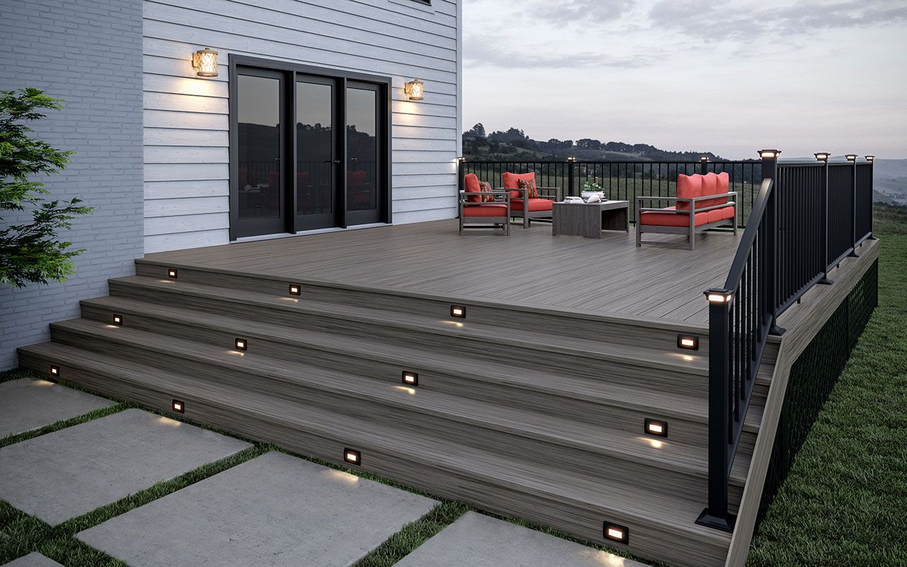 Modern house patio with wide lit steps, deck seating, and black railings overlooking a yard