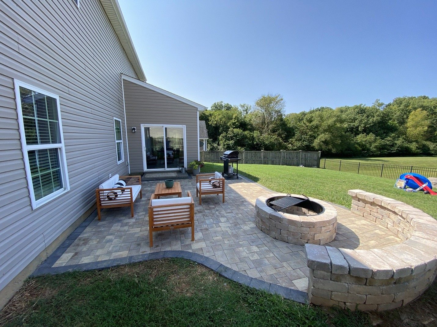 Backyard patio with wicker chairs, fire pit, and curved stone seating beside a house
