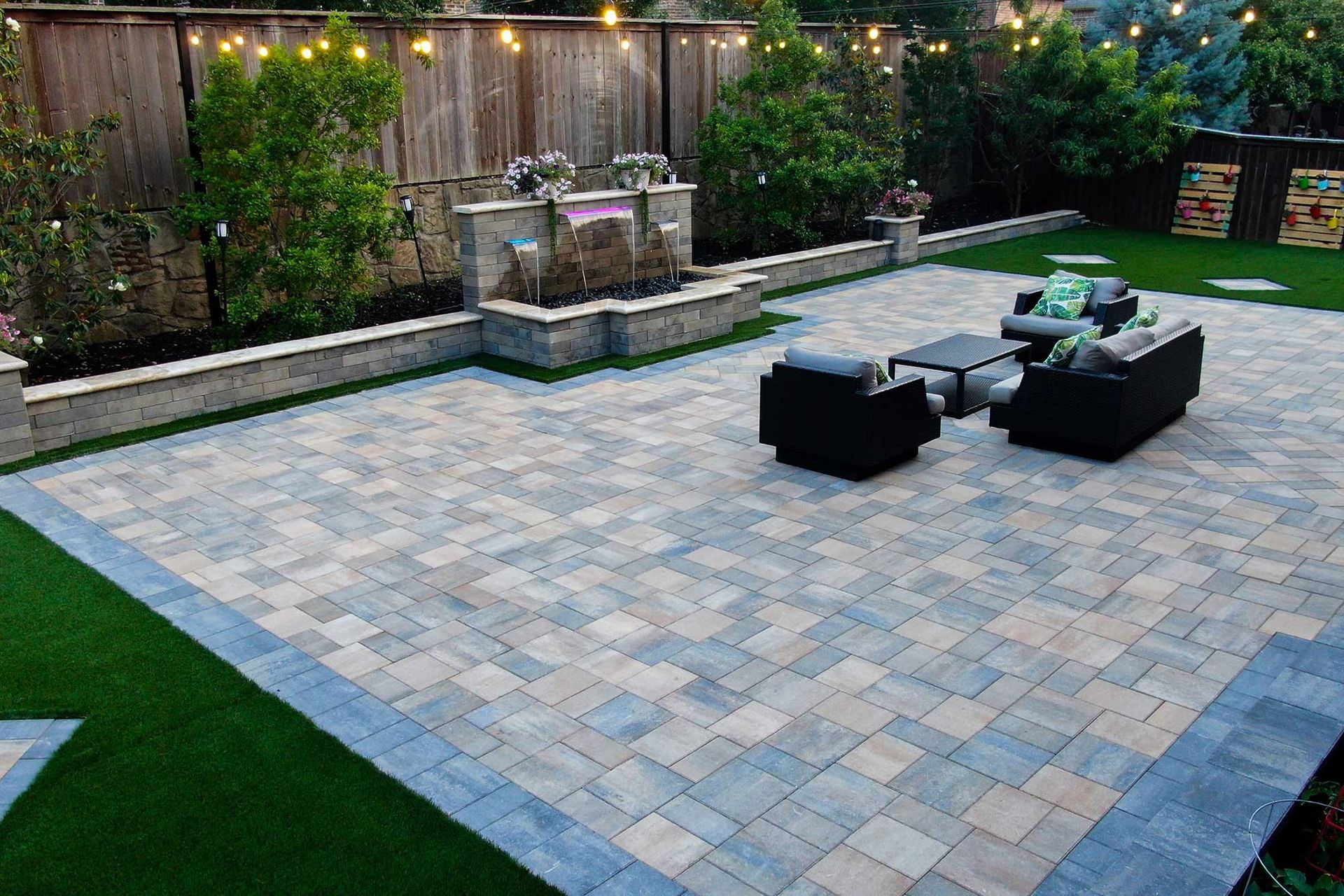 Backyard patio with stone pavers, black seating, and a raised fountain wall at dusk