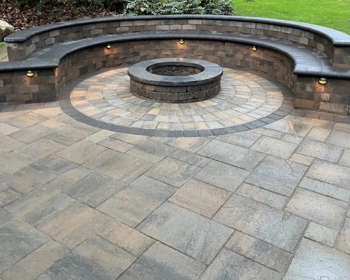Stone patio with a circular fire pit and curved built-in bench seating in a landscaped outdoor area
