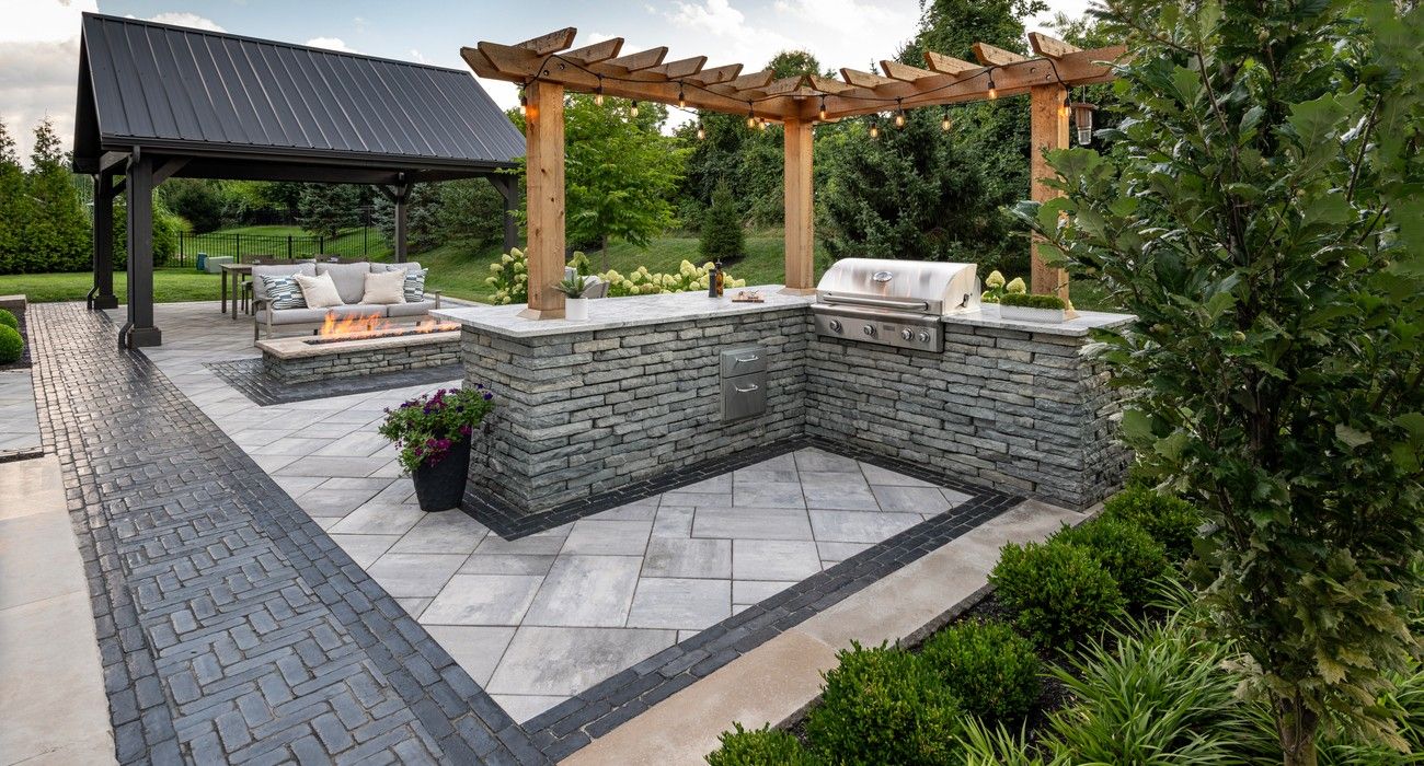 Outdoor patio with stone seating, pergola, built-in grill, and landscaped greenery