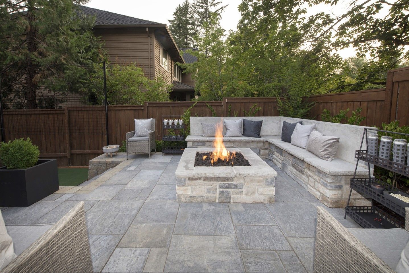 Modern backyard patio with a stone fire pit, curved seating, and trees surrounding it