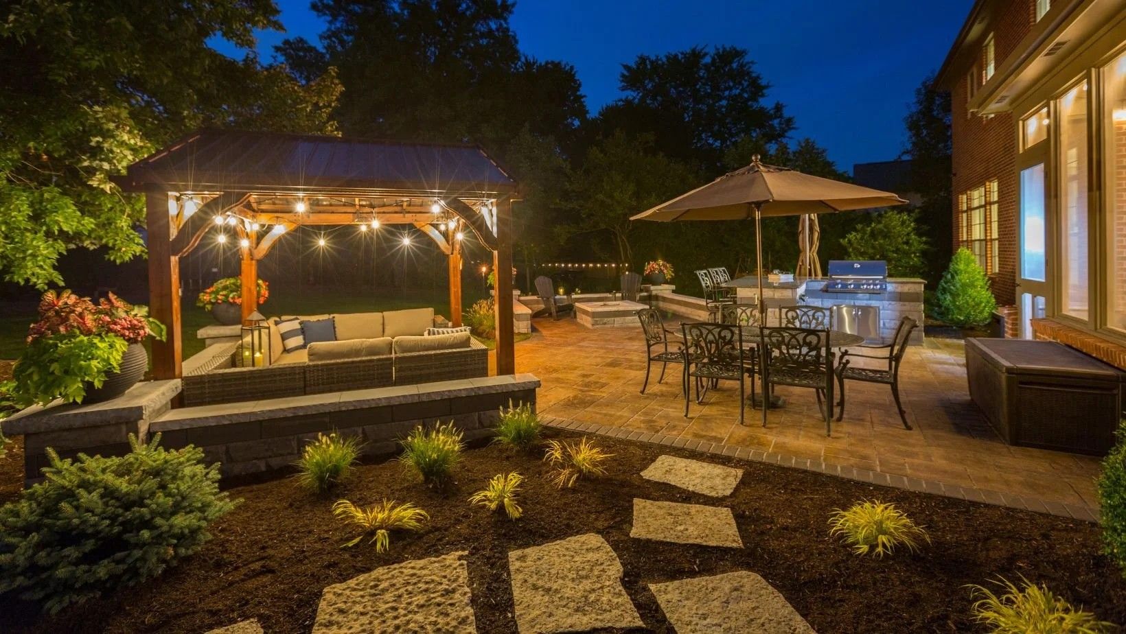Lit backyard patio with gazebo, string lights, stone path, and outdoor dining set at dusk