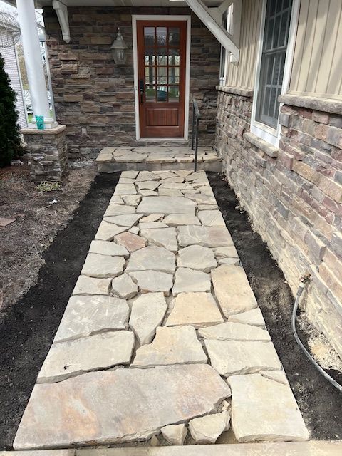 Stone walkway leading to a wooden front door beside a brick house