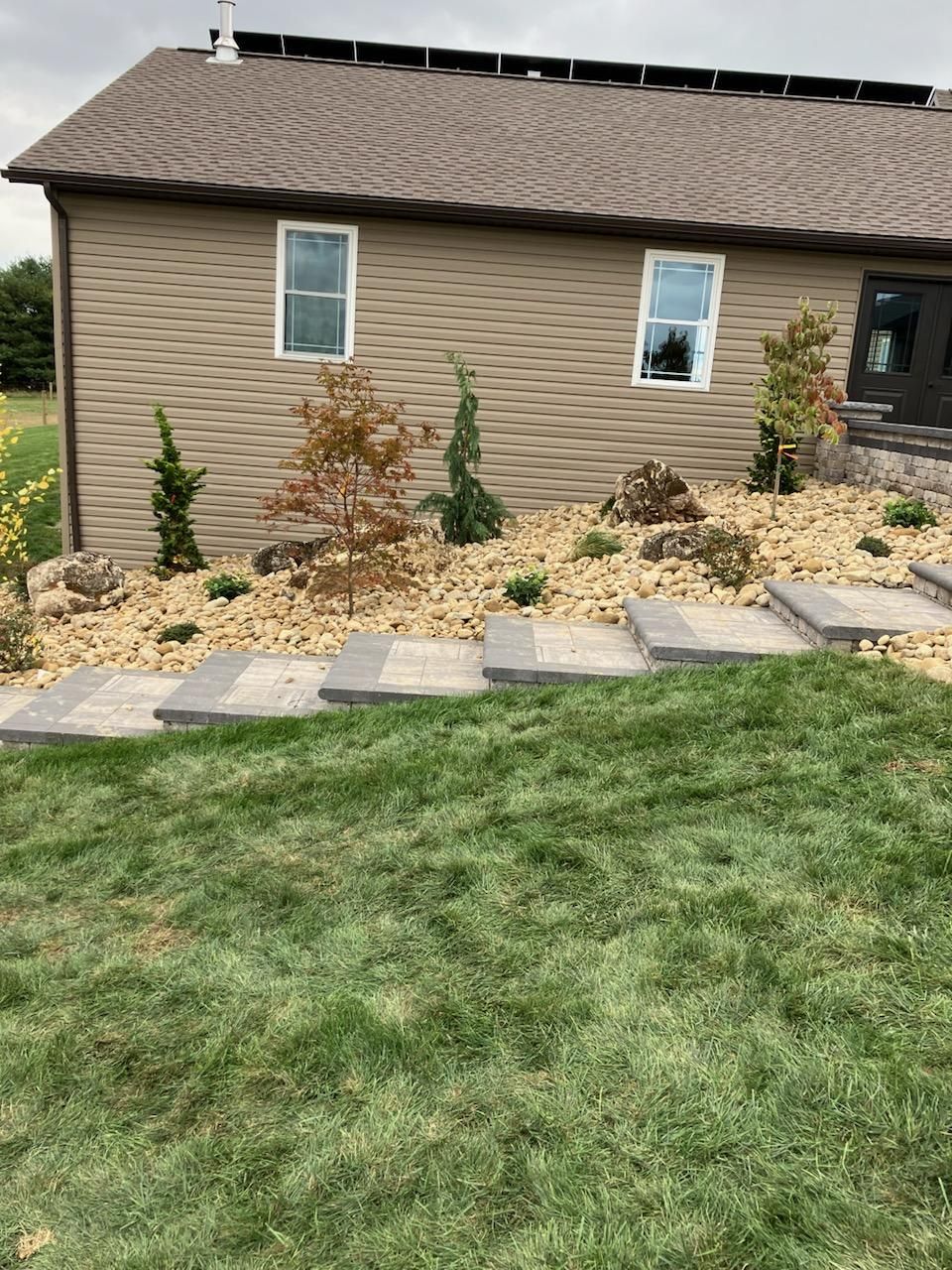 House exterior with tan siding, small windows, stepping stones, and a landscaped front yard with grass and shrubs