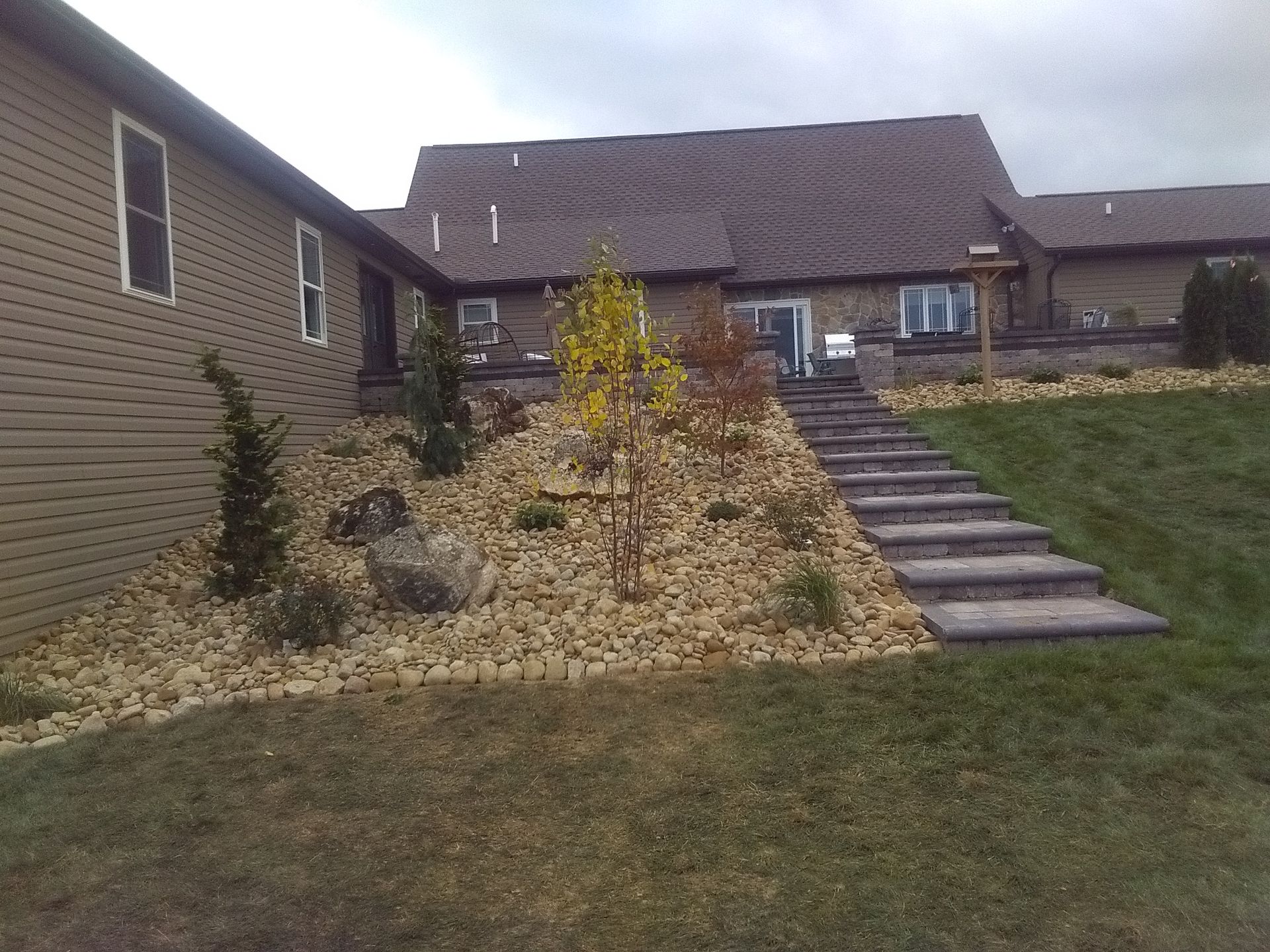 Front yard with stone landscaping, steps up a grassy slope, and a brick house in the background