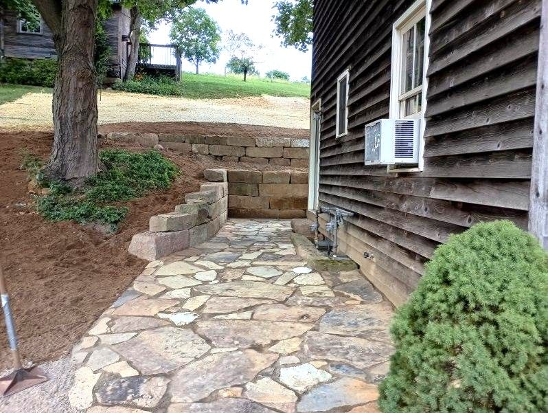 Stone walkway beside a wooden house, with steps up to a yard and trees in the background