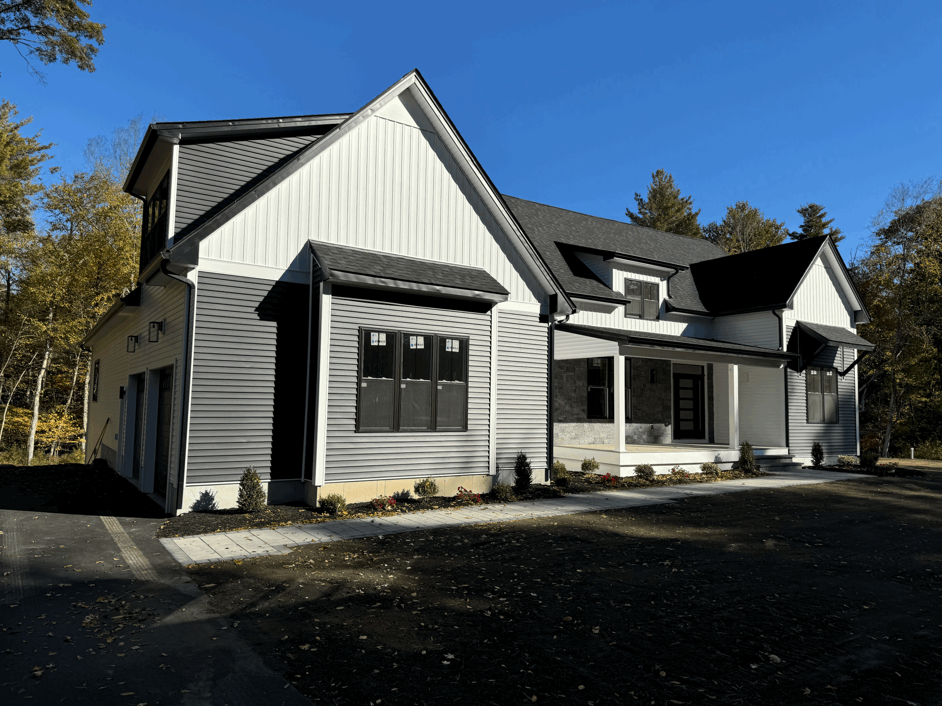 Modern two-story house with black and white siding and a dark roof under a clear blue sky.