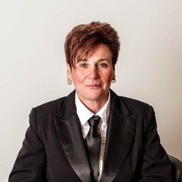 Studio portrait of a person in a dark suit and tie against a plain light background