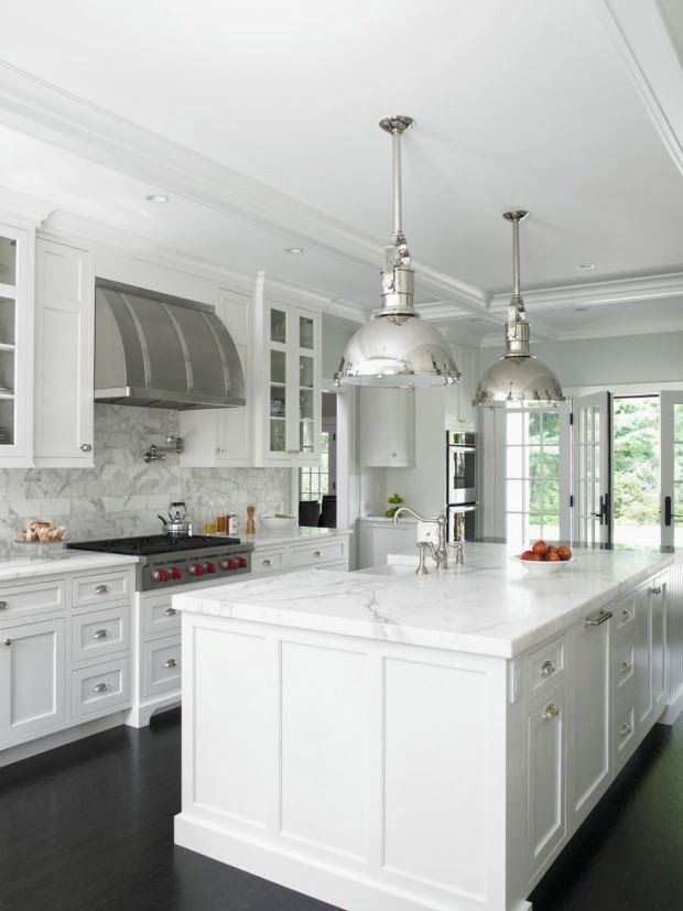 White kitchen with marble countertops, stainless steel fixtures, and large island with hanging lights.