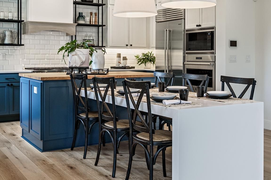 Blue and white kitchen island with wooden countertop, table setting, and black chairs.