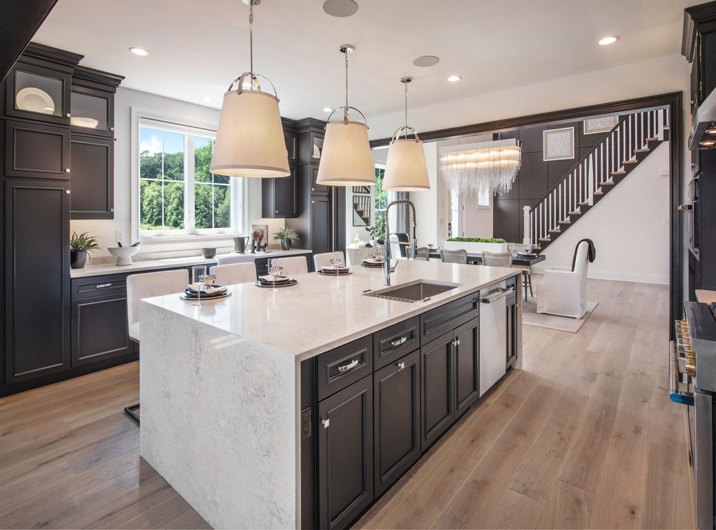 Modern kitchen with dark cabinets, large island, pendant lights, and wooden floors.