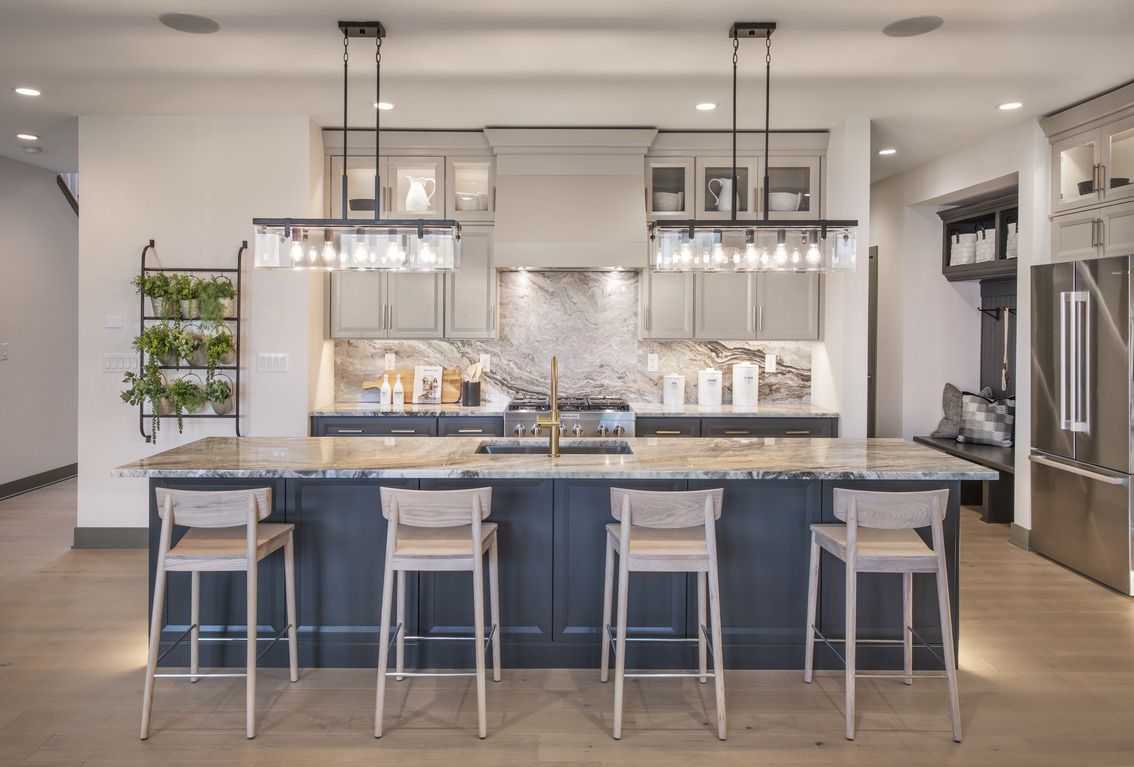 Modern kitchen with a dark island and light-colored stools. Overhead lighting, marble backsplash.