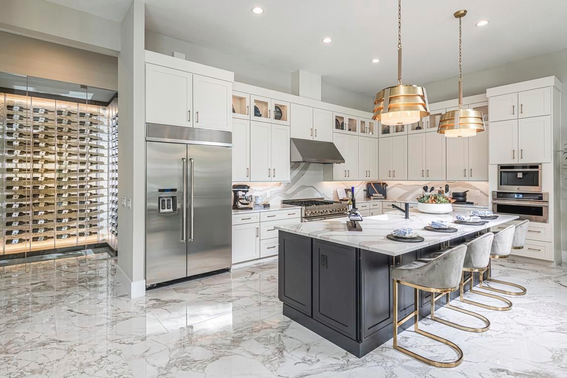 Modern kitchen with white cabinets, marble island, stainless steel appliances, and gold light fixtures.
