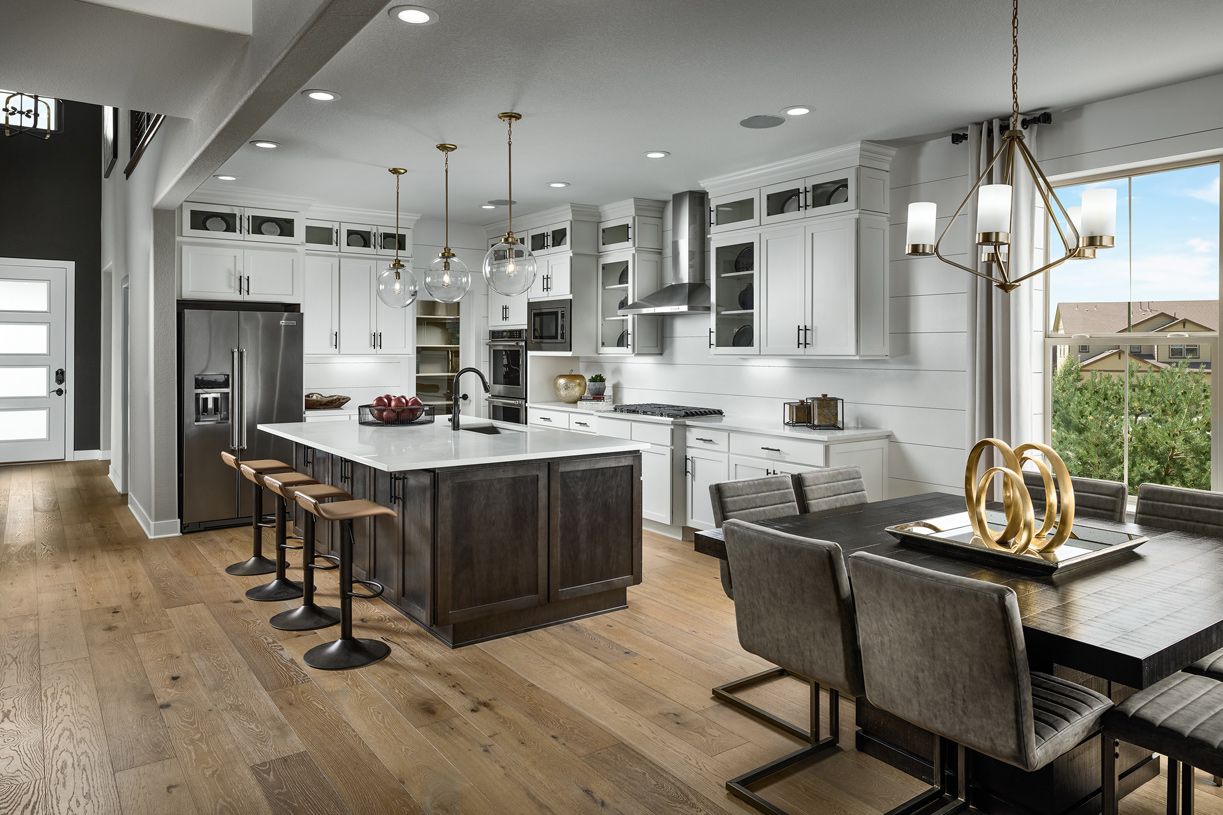 Modern kitchen with white cabinets, dark island, dining area, and hardwood floors.